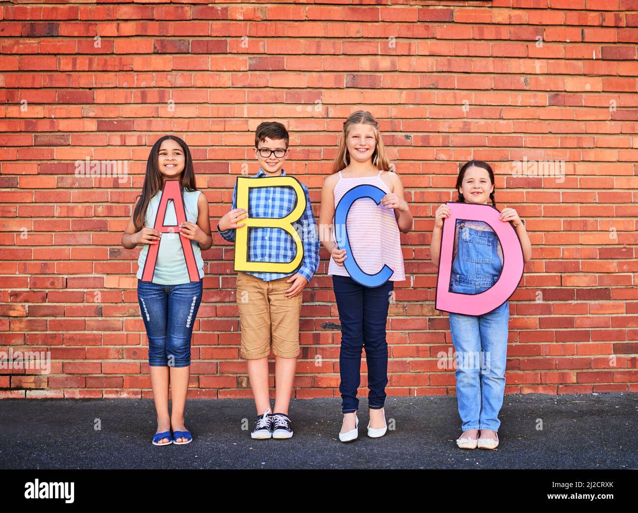 Je mehr Sie wissen, desto mehr wachsen Sie. Porträt einer Gruppe von kleinen Kindern, die Buchstaben aus dem Alphabet an einer Ziegelwand halten. Stockfoto