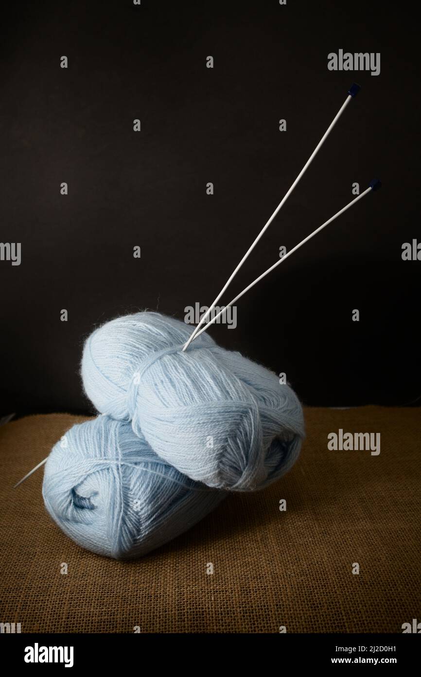 Einige Kugeln aus blauem Garn mit den Stricknadeln, die auf einem schwarzen Hintergrund aufgeklebt sind, kopieren Raum und Seitenlicht Stockfoto