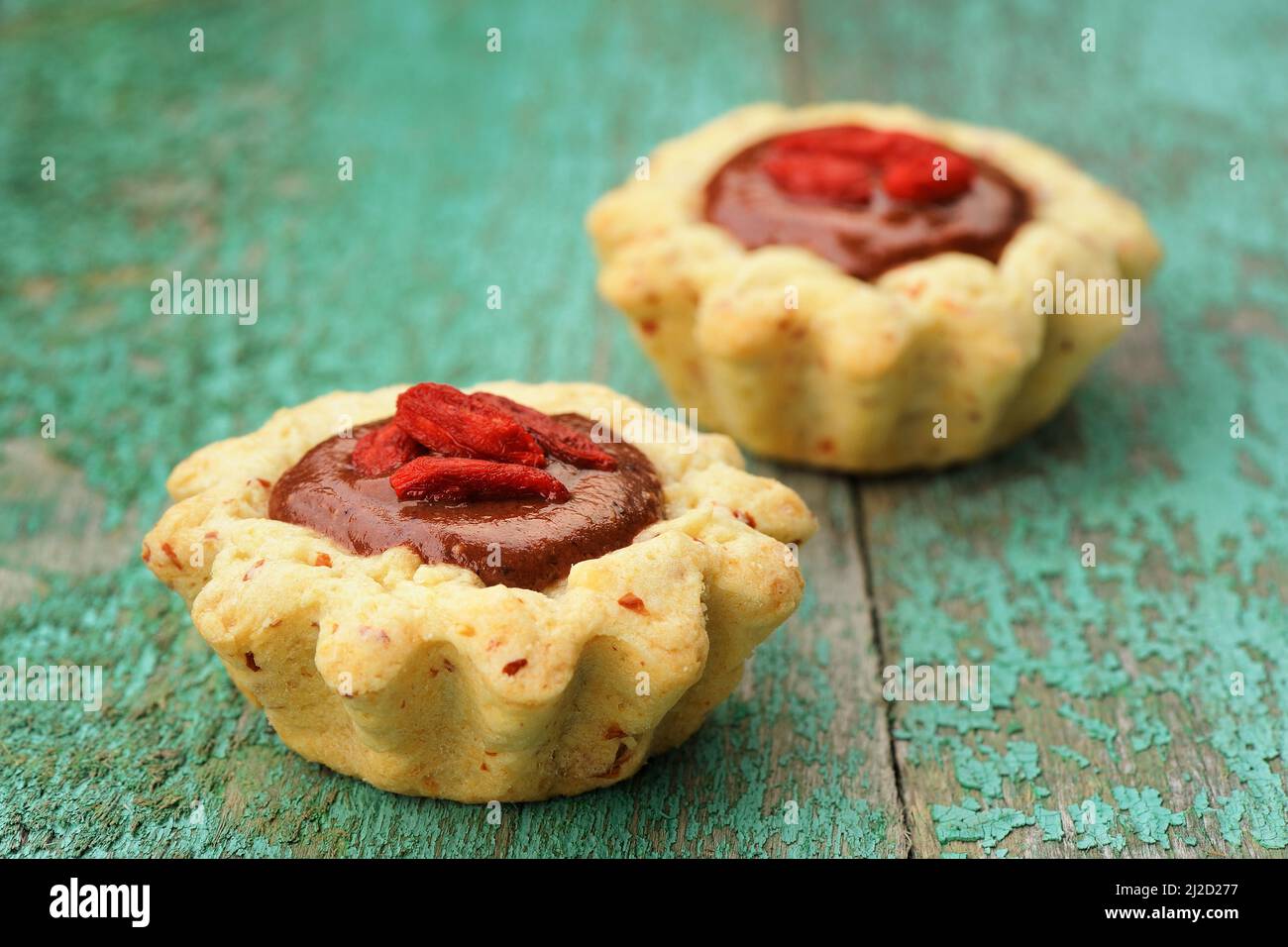 Zwei leckere hausgemachte ausgefallene vegane Kuchen mit Schokoladencreme und trockenen Goji-Beeren auf altem türkisfarbenen Tisch horizontal Nahaufnahme Stockfoto