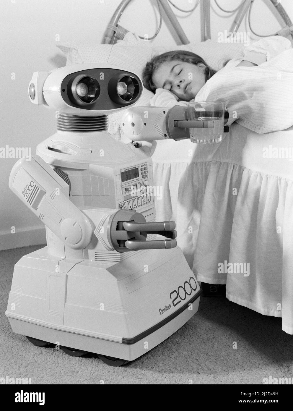Ein junges Mädchen im Bett, das von einem Spielzeug-Roboter Omnibot 2000 geweckt wird. 21.. Oktober 1986. Stockfoto