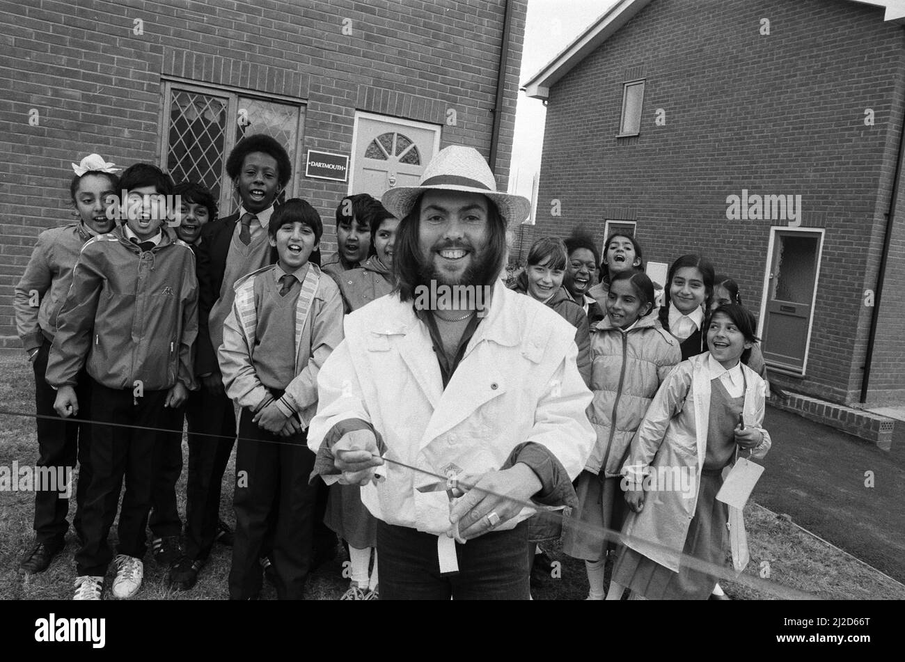 Slade-Star Dave Hill versuchte, das Haus nicht zu „runterbringen“, als er nach 20 Jahren an seinem alten Arbeitsplatz einen Rückbesuch abmachte. Er eröffnete zwei Ausstellungshäuser für eine 67 erarbeitete Bebauung in Heathcroft, Wolverhampton, für Tarmac Houses (Midlands). Im Alter von 18 Jahren war er als Trainee-Käufer für Tarmac tätig, bevor er zum Star wurde. Die Kinder der Farandole Junior School waren vor Ort, um zu sehen, wie Dave das Band durchschneidet - sie haben die Entwicklung und Geschichte des Ortes als Schulprojekt verfolgt. 12.. Juni 1985. Stockfoto