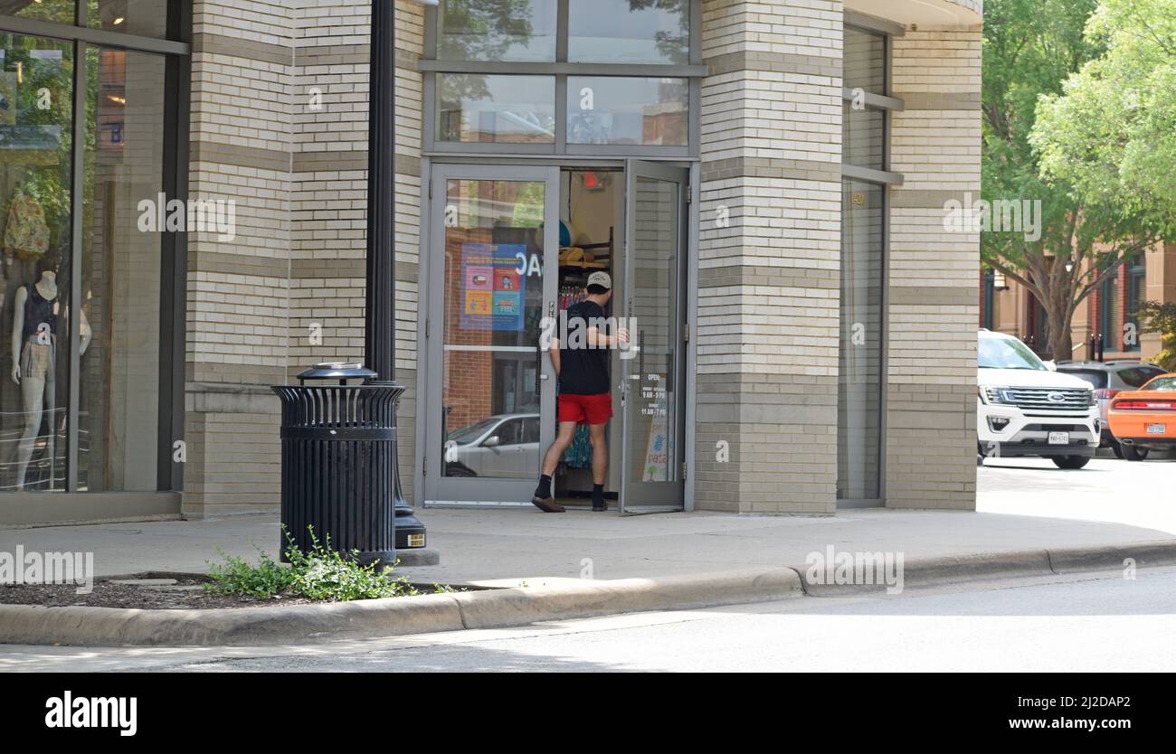 Gen Z-Mann in roten Shorts und schwarzem T-Shirt beim Betreten eines Geschäfts am Southlake Town Square; Southlake, TX Stockfoto