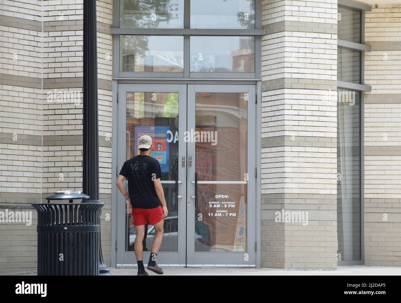 Gen Z Mann in roten Shorts und schwarzem T-Shirt zu einem Geschäft am Southlake Town Square; Southlake, TX Stockfoto