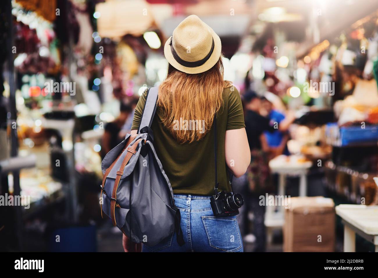 Weiter zum nächsten Wundergebiet. Rückansicht einer unverkennbaren Frau, die einen Hut trägt und tagsüber durch einen belebten Markt im Freien läuft. Stockfoto