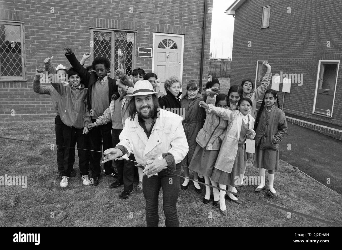 Slade-Star Dave Hill versuchte, das Haus nicht zu „runterbringen“, als er nach 20 Jahren an seinem alten Arbeitsplatz einen Rückbesuch abmachte. Er eröffnete zwei Ausstellungshäuser für eine 67 erarbeitete Bebauung in Heathcroft, Wolverhampton, für Tarmac Houses (Midlands). Im Alter von 18 Jahren war er als Trainee-Käufer für Tarmac tätig, bevor er zum Star wurde. Die Kinder der Farandole Junior School waren vor Ort, um zu sehen, wie Dave das Band durchschneidet - sie haben die Entwicklung und Geschichte des Ortes als Schulprojekt verfolgt. 12.. Juni 1985. Stockfoto