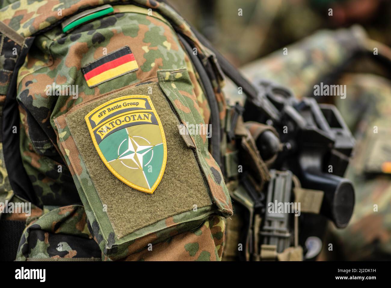 Flagge Deutschlands und Symbol der NATO-Kampfgruppe auf Soldatenuniform mit Schrotflinte oder Gewehr, NATO-Einheit zur Integration, Nahaufnahme Stockfoto