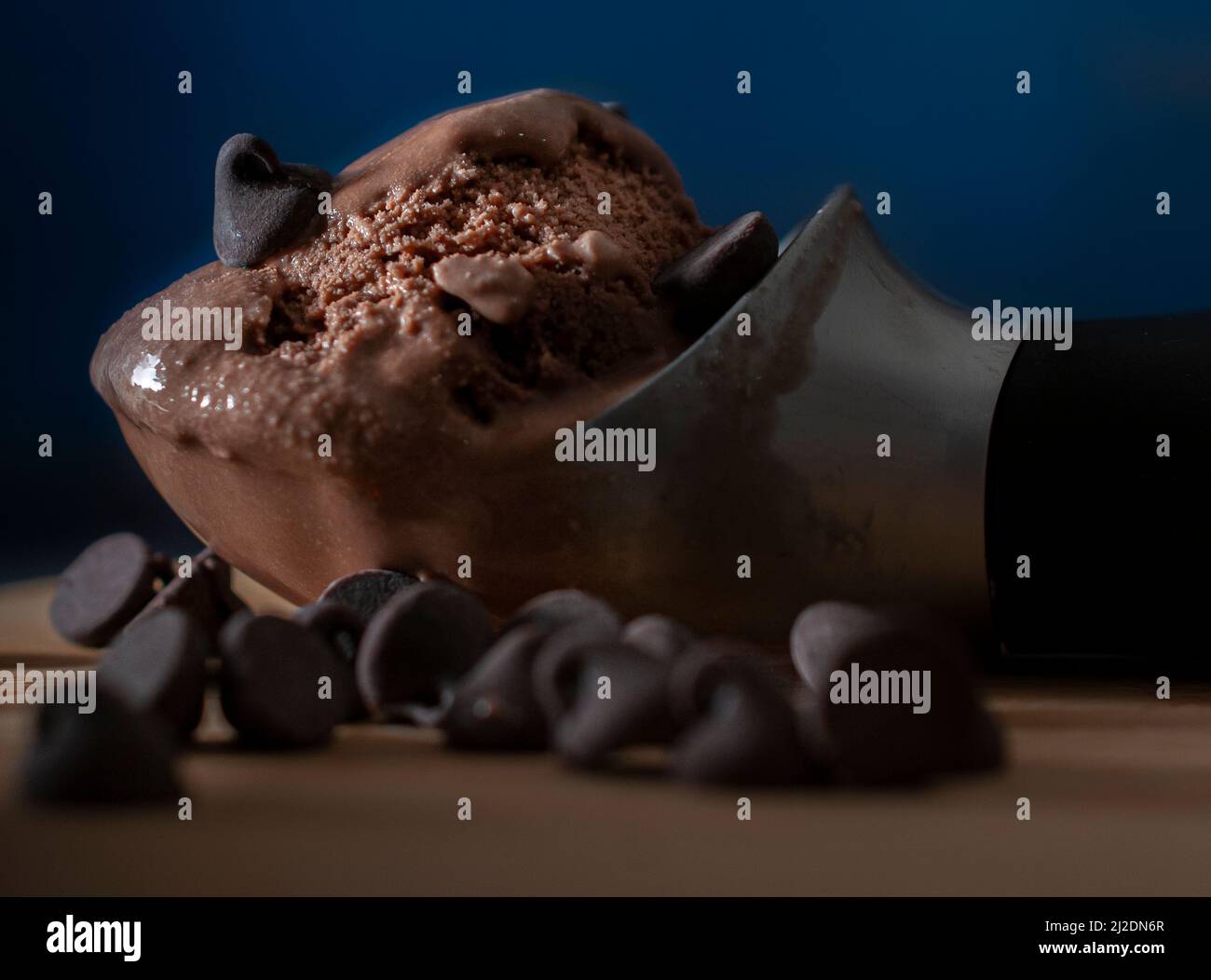 Schokoladeneis auf einem Löffel mit Schokoladensplittern auf der Seite und einem dunkelblauen Hintergrund Seitenansicht Makro-dunkle Lebensmittel-Fotografie Stockfoto