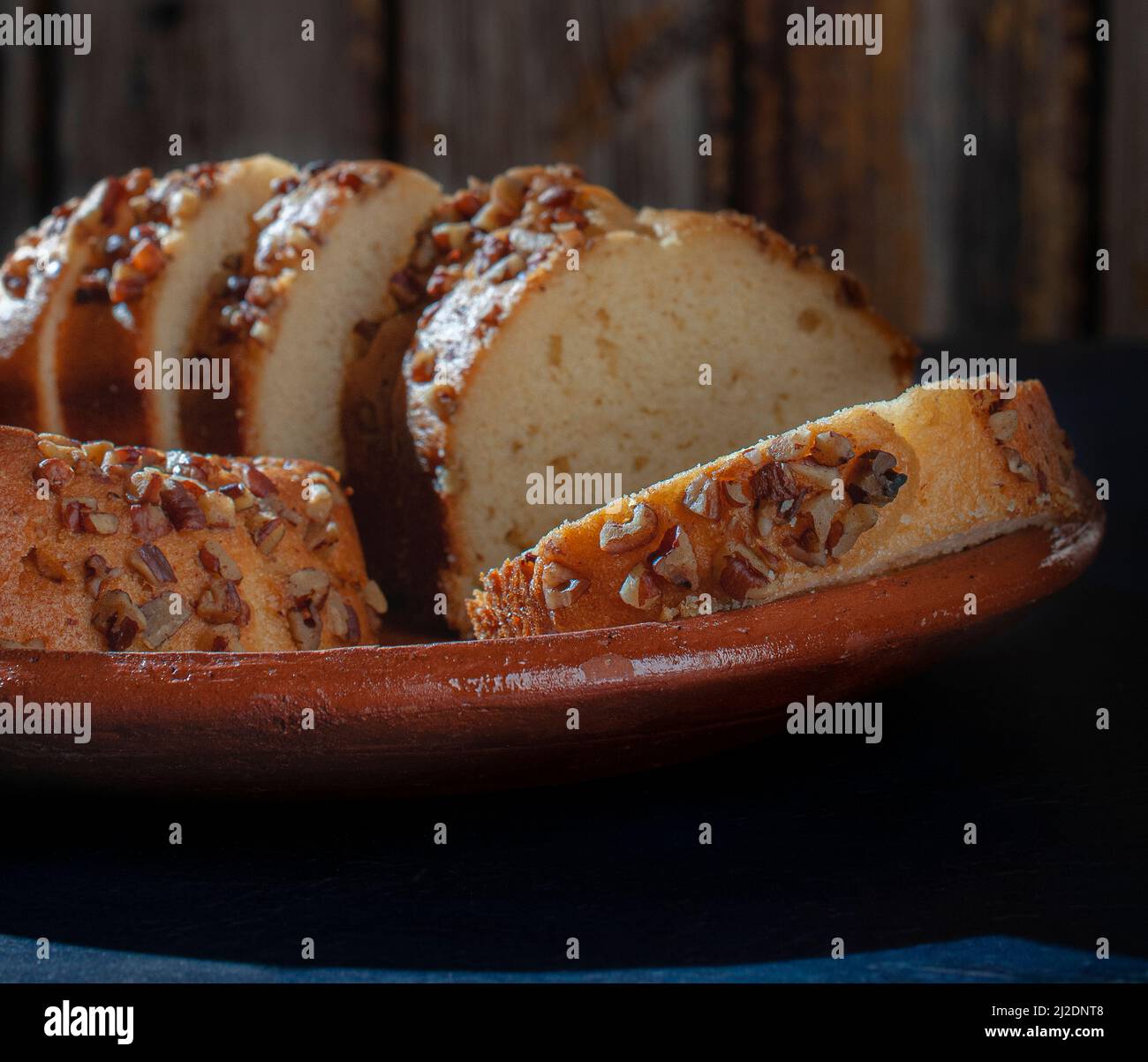 Süße Brotscheiben mit Walnüssen darauf, auf einem mexikanischen Teller mit Schlamm oder Lehm und einem blauen Tisch Stockfoto