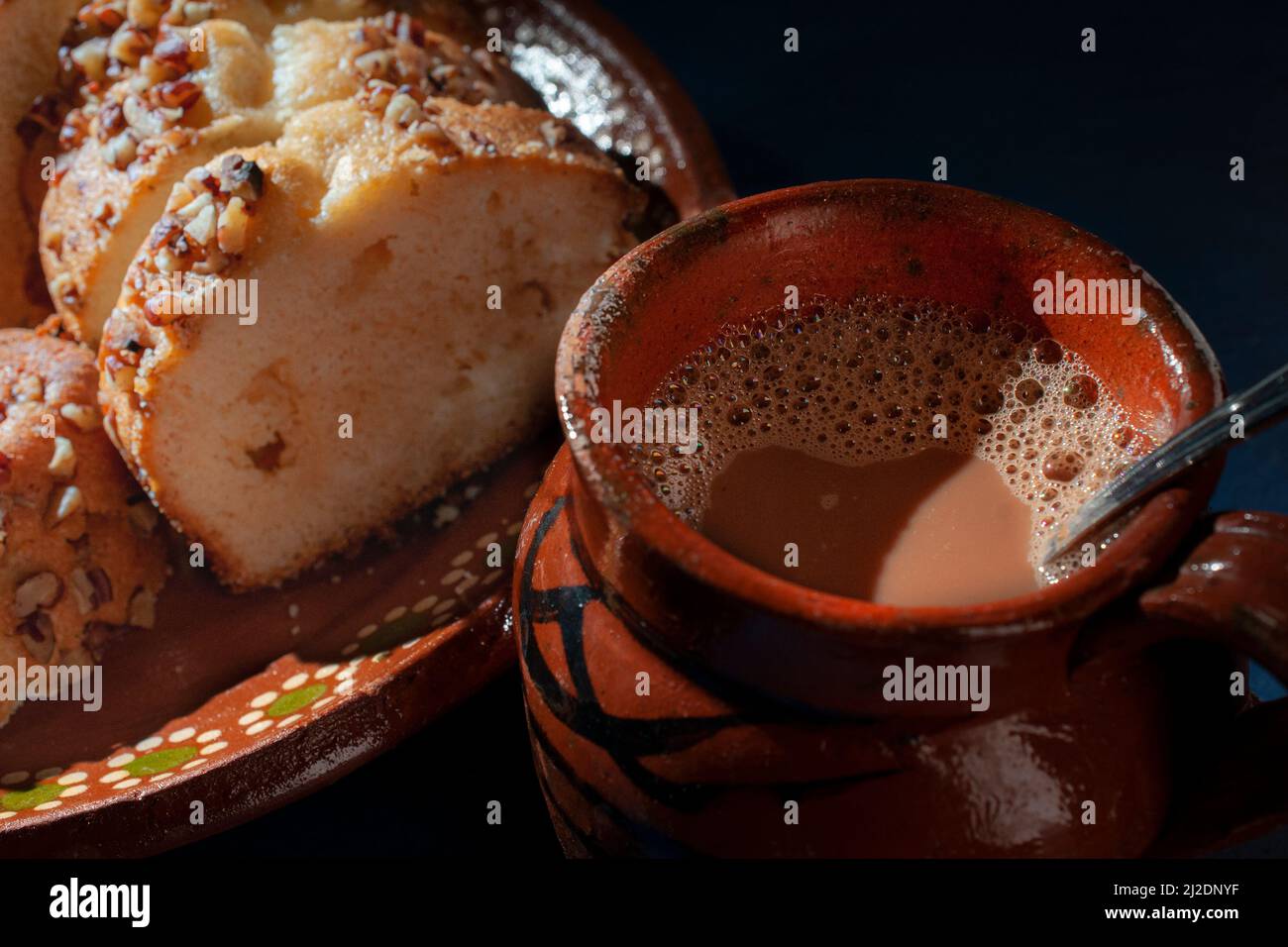 Süße Brotscheiben mit Walnussstücken darauf, auf einem mexikanischen Teller mit Schlamm oder Lehm und einer heißen Tasse Kaffee oder Schokolade auf der Seite Stockfoto