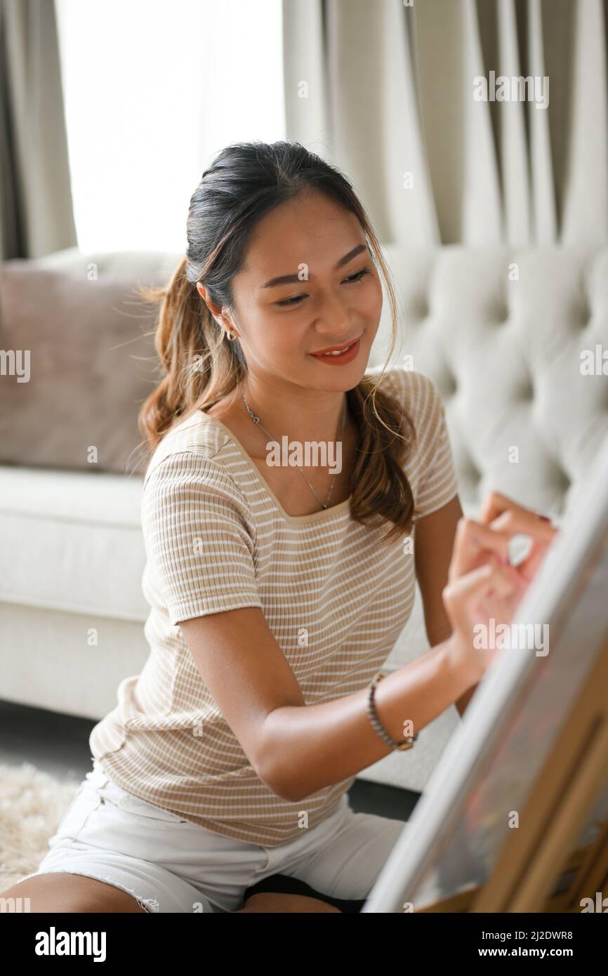 Portrait, Eine charmante asiatische Frau zeichnet ihr inspiriertes Bild auf eine Leinwand. Kreative Hobbys. Stockfoto