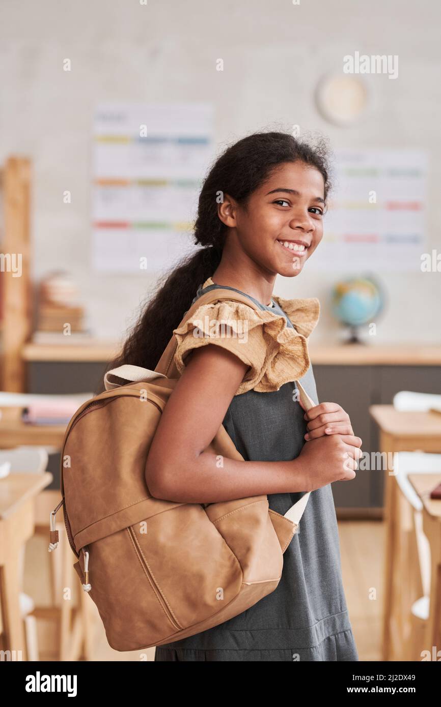 Vertikales Porträt eines lächelnden afroamerikanischen Mädchens in der Schule, das im Klassenzimmer auf die Kamera schaut Stockfoto