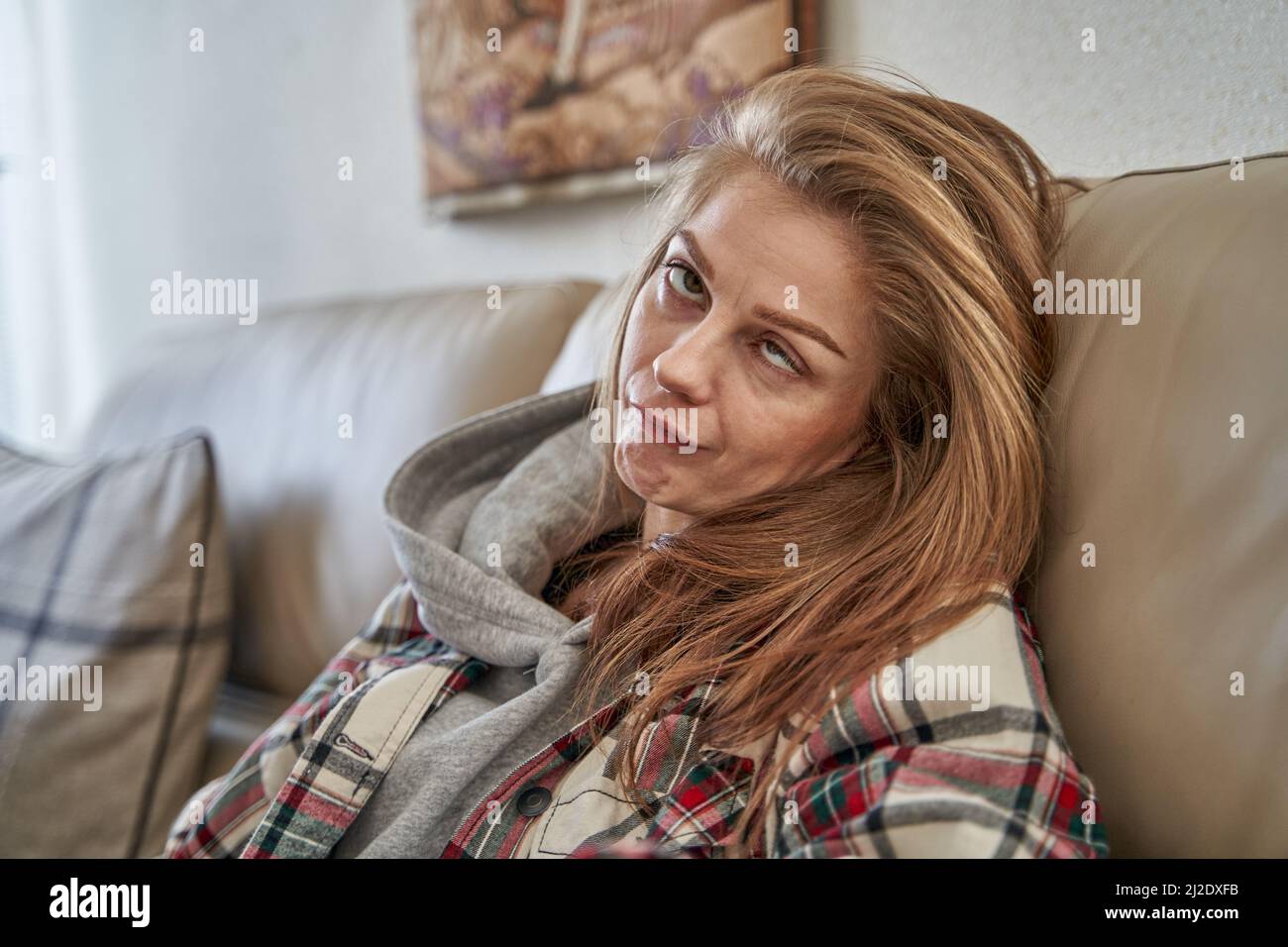 Eine junge kaukasische Frau sitzt auf dem Sofa und grimazing Stockfoto
