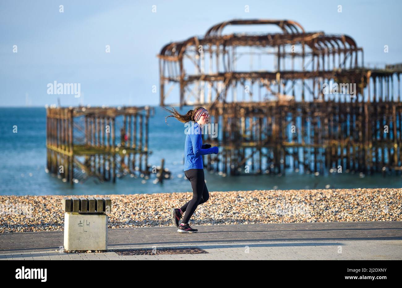 Brighton UK 1. April 2022 - Ein Läufer kommt an einem sonnigen, aber kalten Morgen am West Pier in Brighton vorbei und hat wieder Schneevorhersagen für einige Teile Großbritanniens: Credit Simon Dack / Alamy Live News Stockfoto