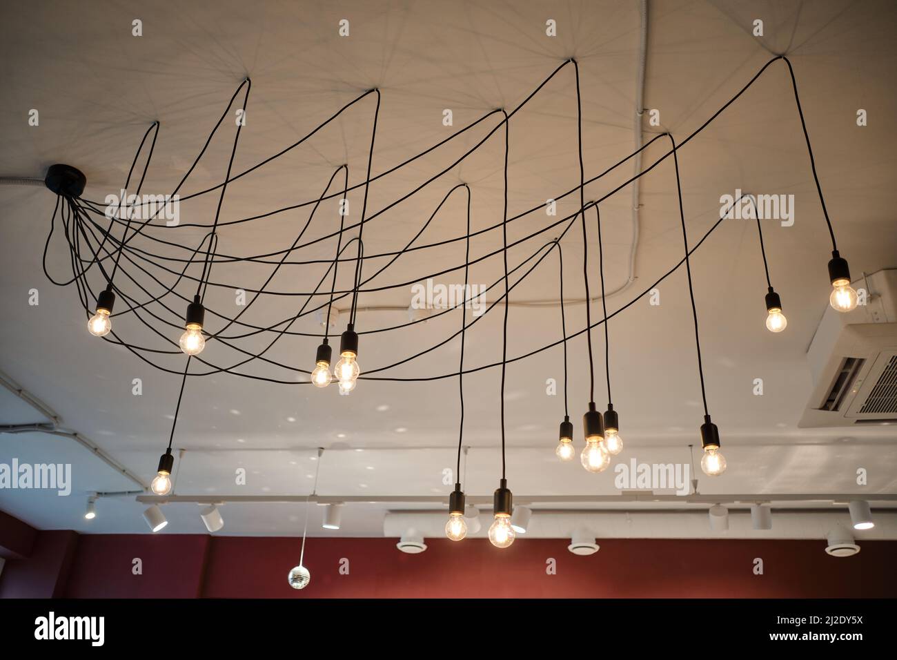 Ungewöhnlicher Kronleuchter mit individuellen Glühbirnen schmückt die Decke im gemütlichen Café. Lampen beleuchten großen Raum und erzeugen interessante Wirkung. Stockfoto