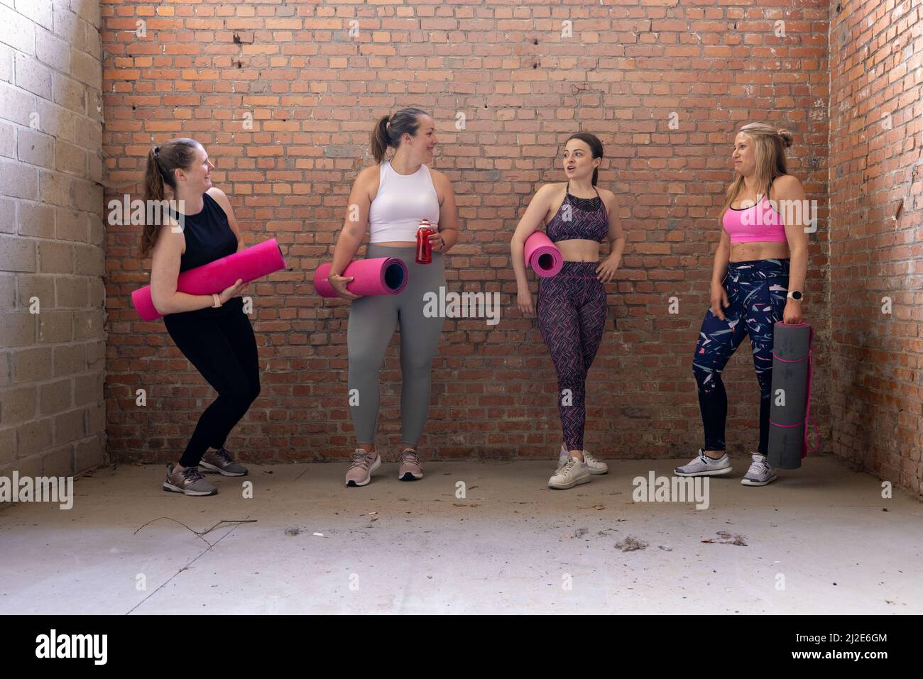 Eine Gruppe junger, attraktiver, sportlicher Frauen unterschiedlicher Körperformen versammelten sich und sprachen während des Wartens im Fitnessstudio. Industrielle Backsteinmauer Hintergrund. Hochwertige Fotos Stockfoto