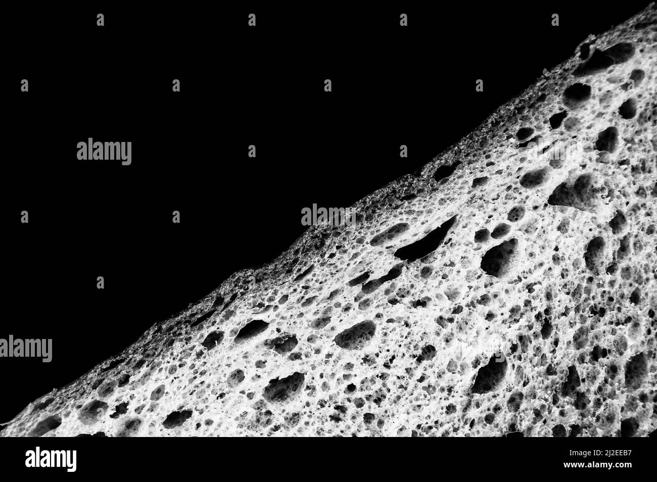 Scheibe Weißbrot Nahaufnahme isoliert auf schwarzem Hintergrund. Grau rau strukturierte Oberfläche gehackt Stück Laib von Lebensmitteln mit Löchern. Draufsicht. Abstract Konz Stockfoto