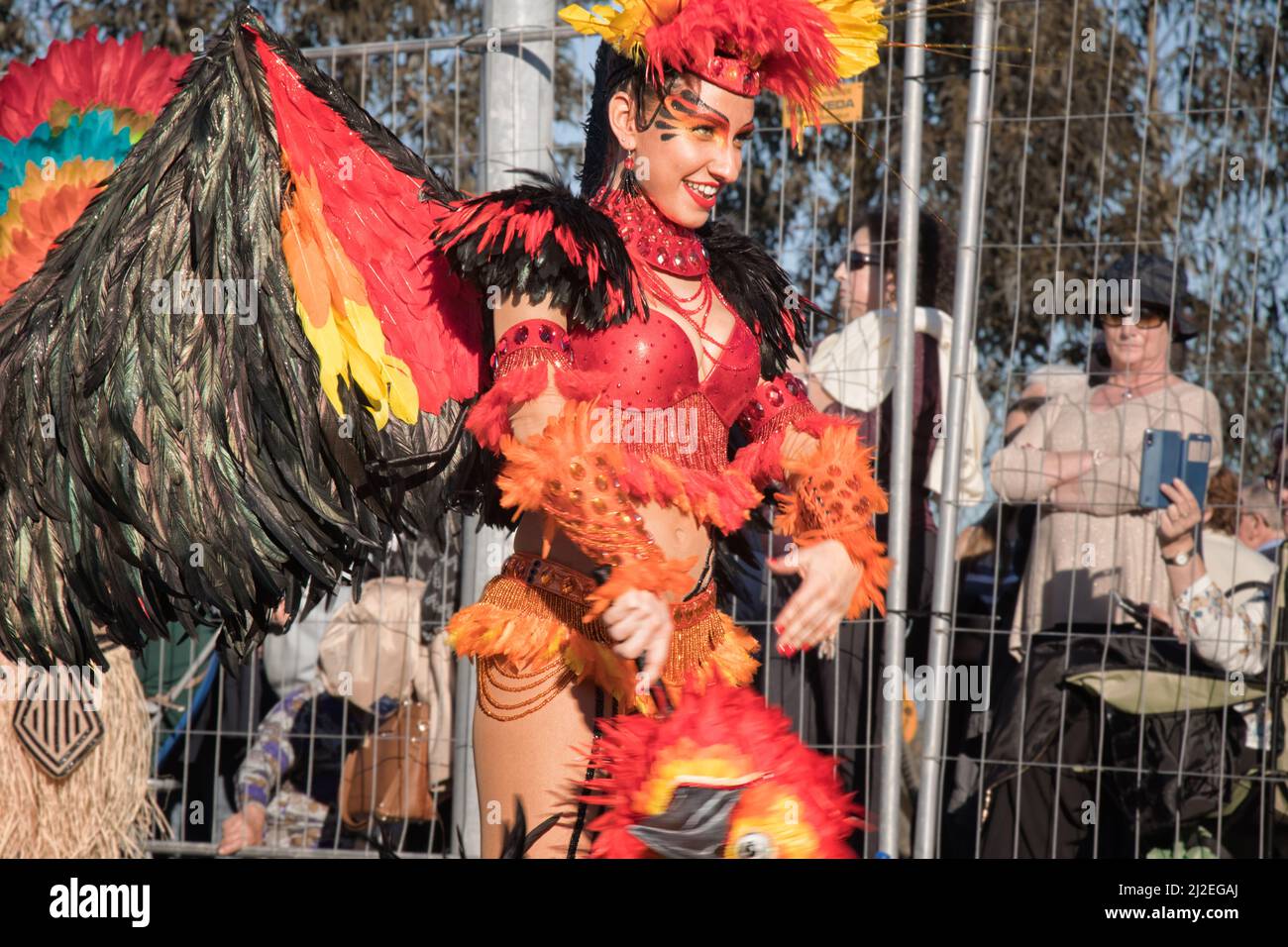 Portugal Karneval, lächelnde Frau in einem roten, gelben und schwarzen Vogel-Kostüm - Ovar, Grande Desfile. Große Parade, einige Spekulatoren. Stockfoto