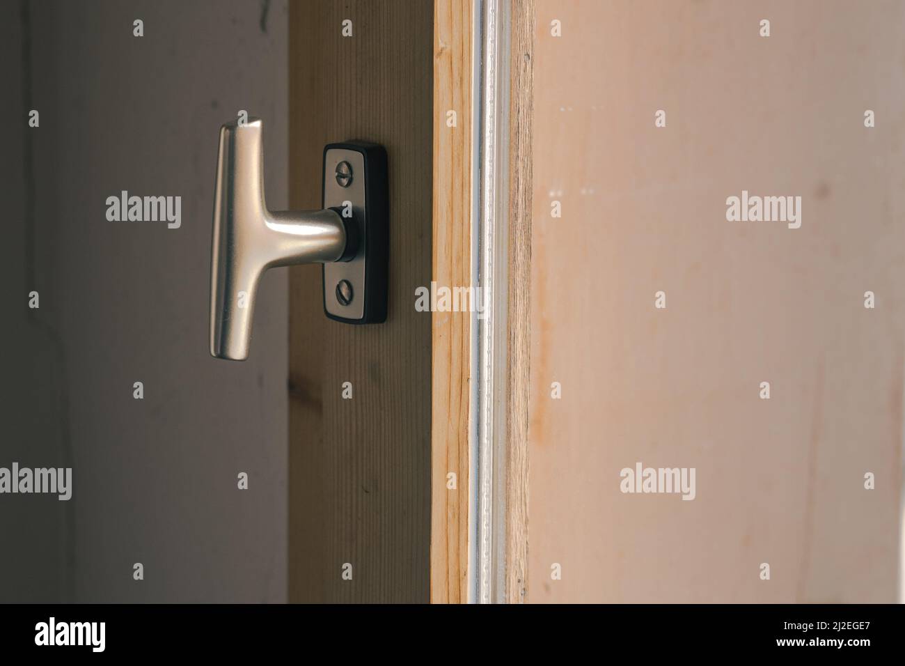 Typischer Fensterknopf, der in geschlossener Position auf einem Holzfensterrahmen montiert ist. Moderner Metallknopf oder Haken zum Öffnen des Fensters. Stockfoto