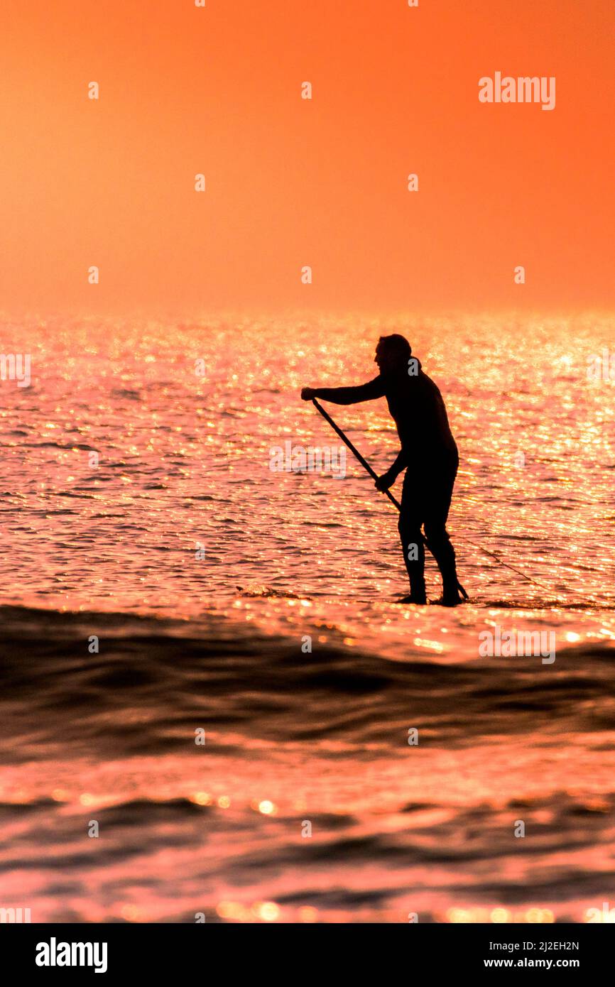 Ein Paddelboarder, der von einem spektakulären Sonnenuntergang am Fistral Beach am Ende des wärmsten Tages des Jahres in Newquay in Cornwall in Großbritannien umrast wird. Stockfoto