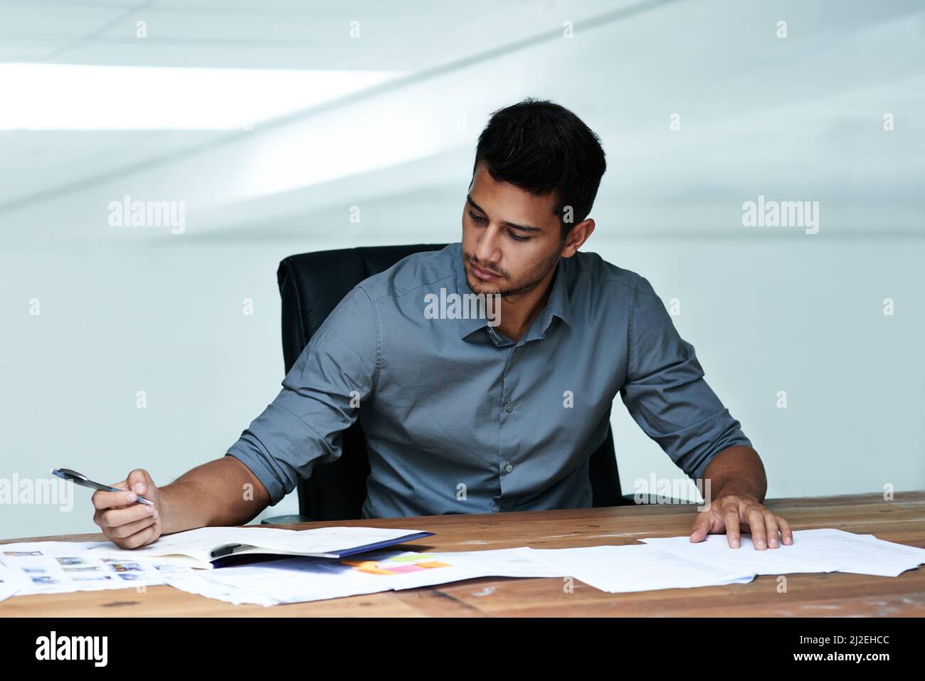 Hart arbeiten, um die Fristen einzuhalten. Eine kleine Aufnahme eines hübschen jungen Geschäftsmannes, der während der Arbeit in einem modernen Büro Schreibarbeit leistet. Stockfoto