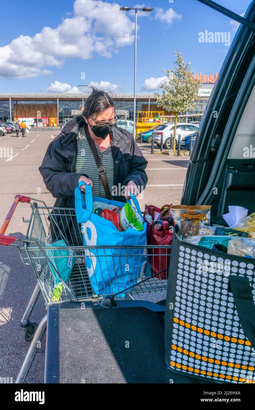 Frau, die ihren wöchentlichen Laden vom Trolley auf einem Supermarkt-Parkplatz in die Rückseite ihres Autos entlädt. NB: Model Release für Person im Vordergrund verfügbar Stockfoto
