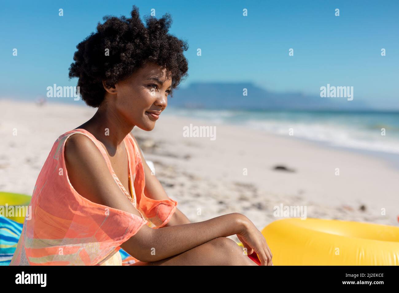 afroamerikanische Frau mit schwarzer Afro-Frisur sitzt am Strand und genießt den Sommerurlaub Stockfoto