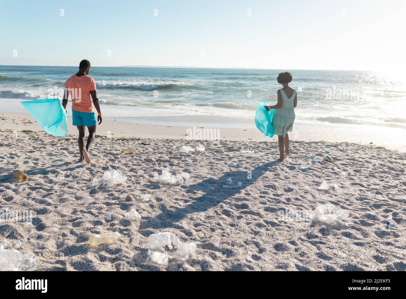 afroamerikanisches Paar sammelt an sonnigen Tagen Plastikmüll am Strand in einem Beutel Stockfoto