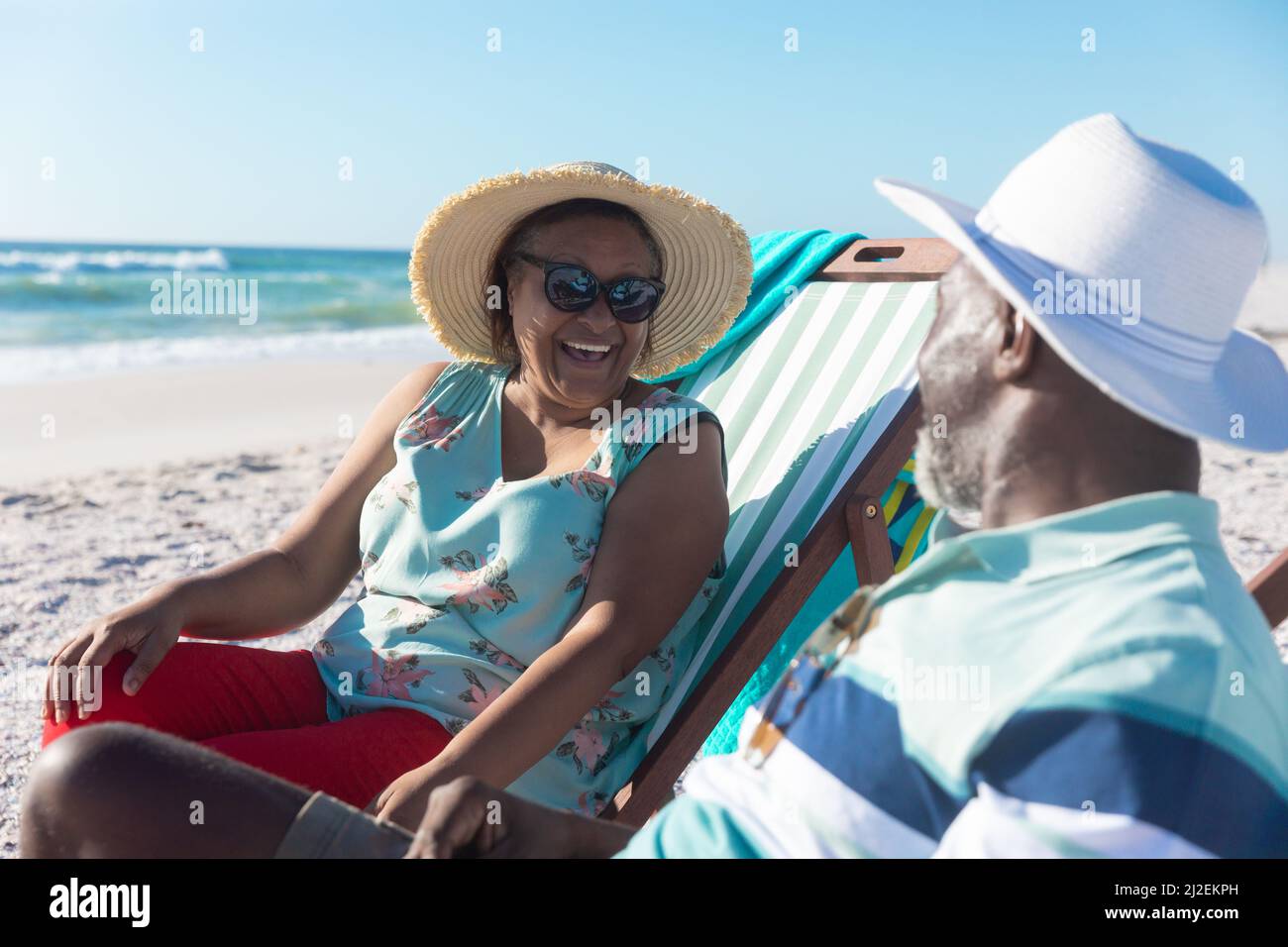 Ein glückliches afroamerikanisches Seniorenpaar, das sich auf Klappstühlen am Strand unterhielt Stockfoto