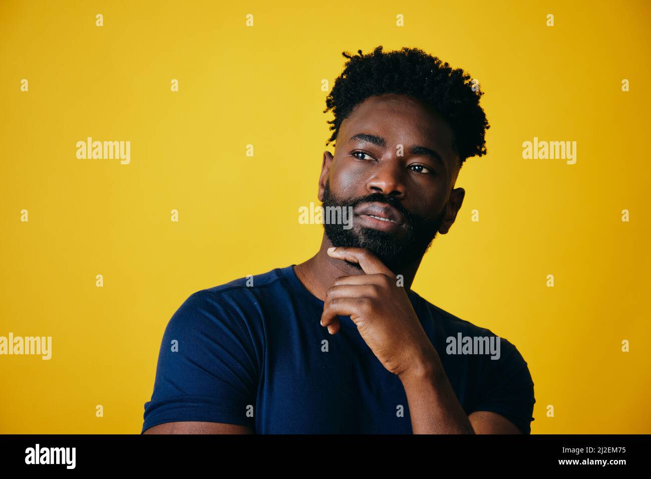 Nachdenklicher Afro-Mann mit der Hand am Kinn, der vor gelbem Hintergrund absieht Stockfoto