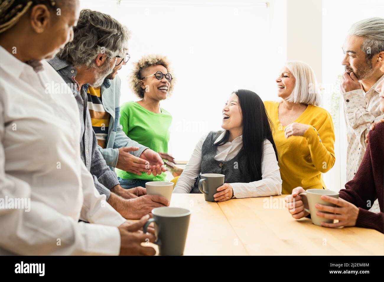 Fröhliche, multirassische Menschen mit unterschiedlichen Alters und Ethnien, die zu Hause eine Tasse Kaffee trinken Stockfoto
