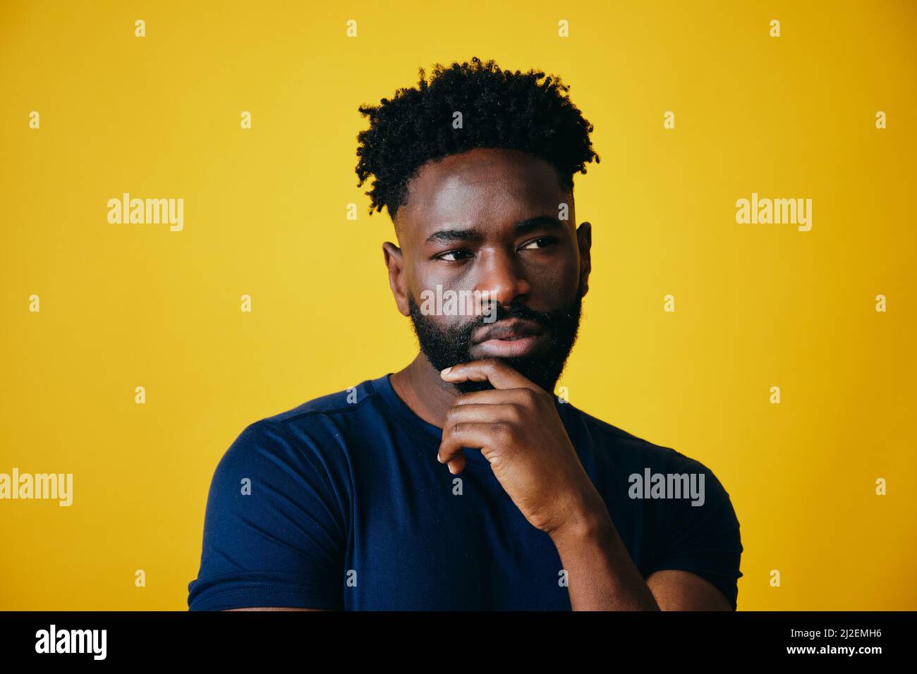 Nachdenklicher Afro-Mann mit der Hand am Kinn, der vor gelbem Hintergrund absieht Stockfoto