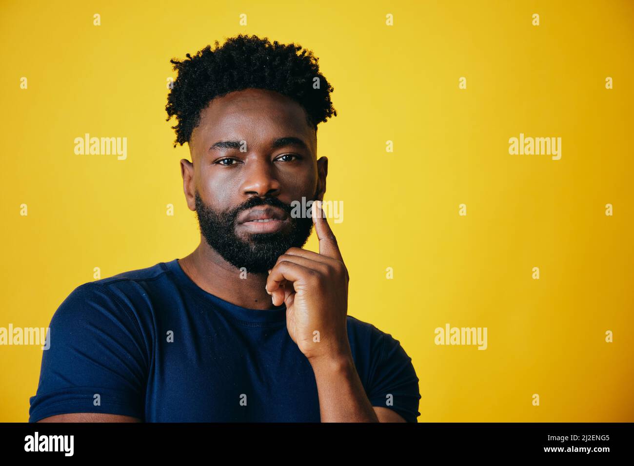 Nachdenklicher Afro-Mann mit der Hand am Kinn und Blick auf die Kamera vor gelbem Hintergrund Stockfoto
