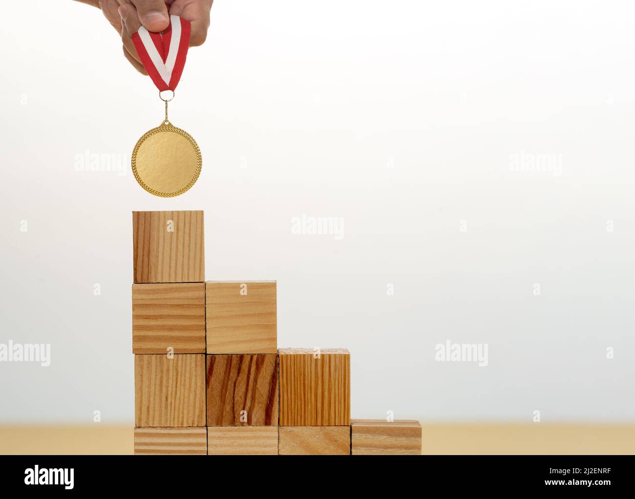 Steigleiter aus Holzblöcken auf der obersten goldenen Medaille als Symbol für AIM Ambition Motivation auf Erfolg. Stockfoto