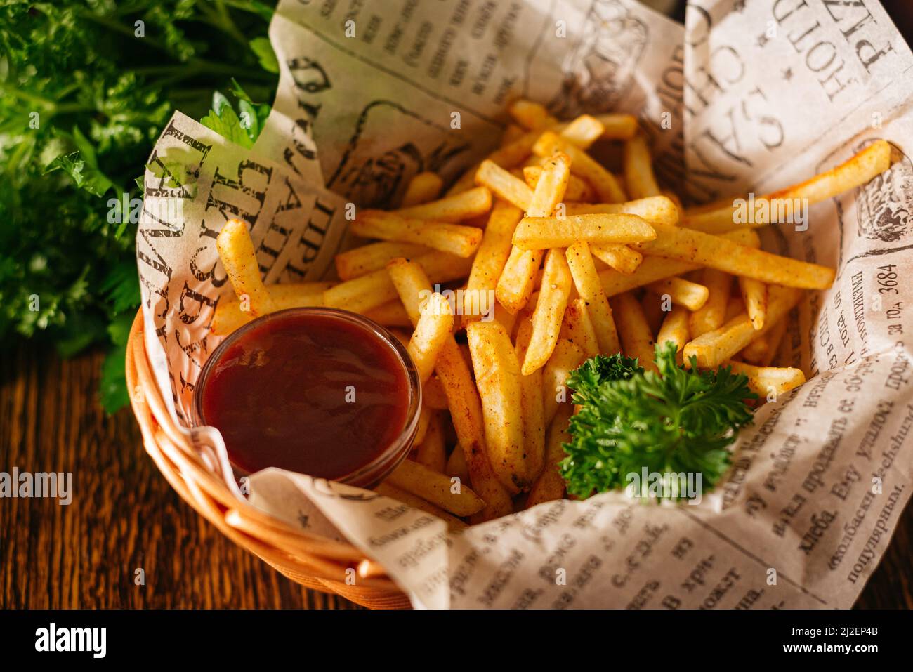 Portion Pommes Frites und Ketchup-Sauce. Das Essen an der Bar wird in einem Korb serviert. Knusprige Pommes mit Petersilienblättern. Stockfoto