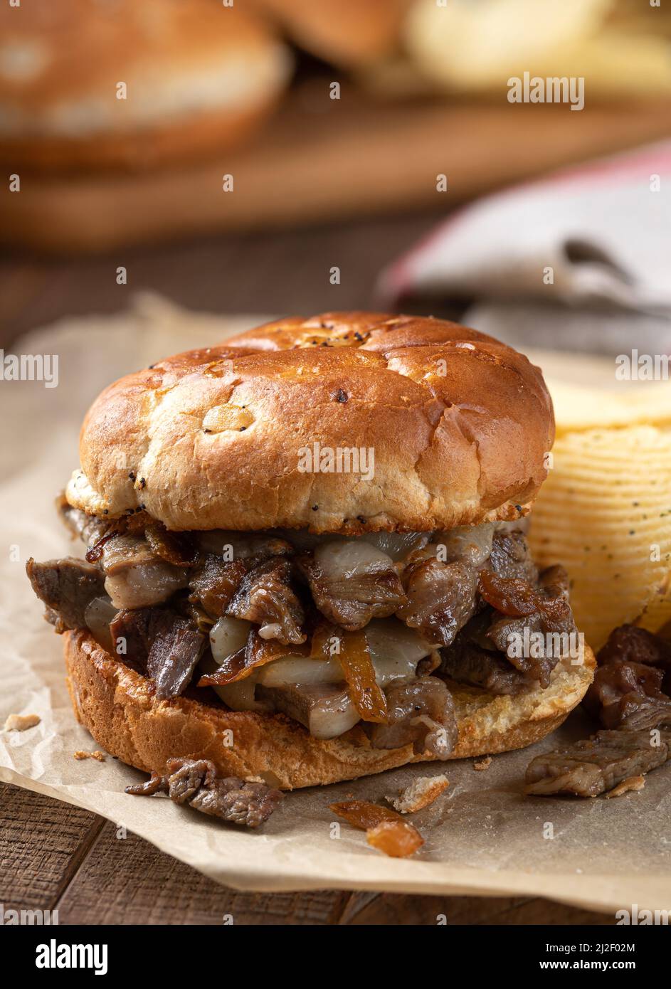 Heißes Käsesteak-Sandwich auf einem getoasteten Brötchen mit Kartoffelchips auf einem rustikalen Holztisch Stockfoto