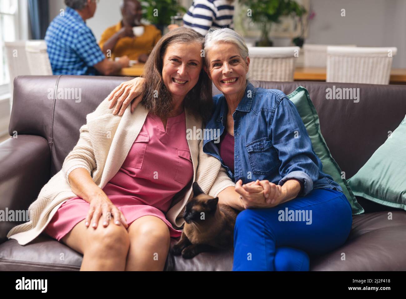 Porträt einer lächelnden kaukasischen älteren Freundin, die die Hände hält, während sie mit einer Katze auf dem Sofa sitzt Stockfoto