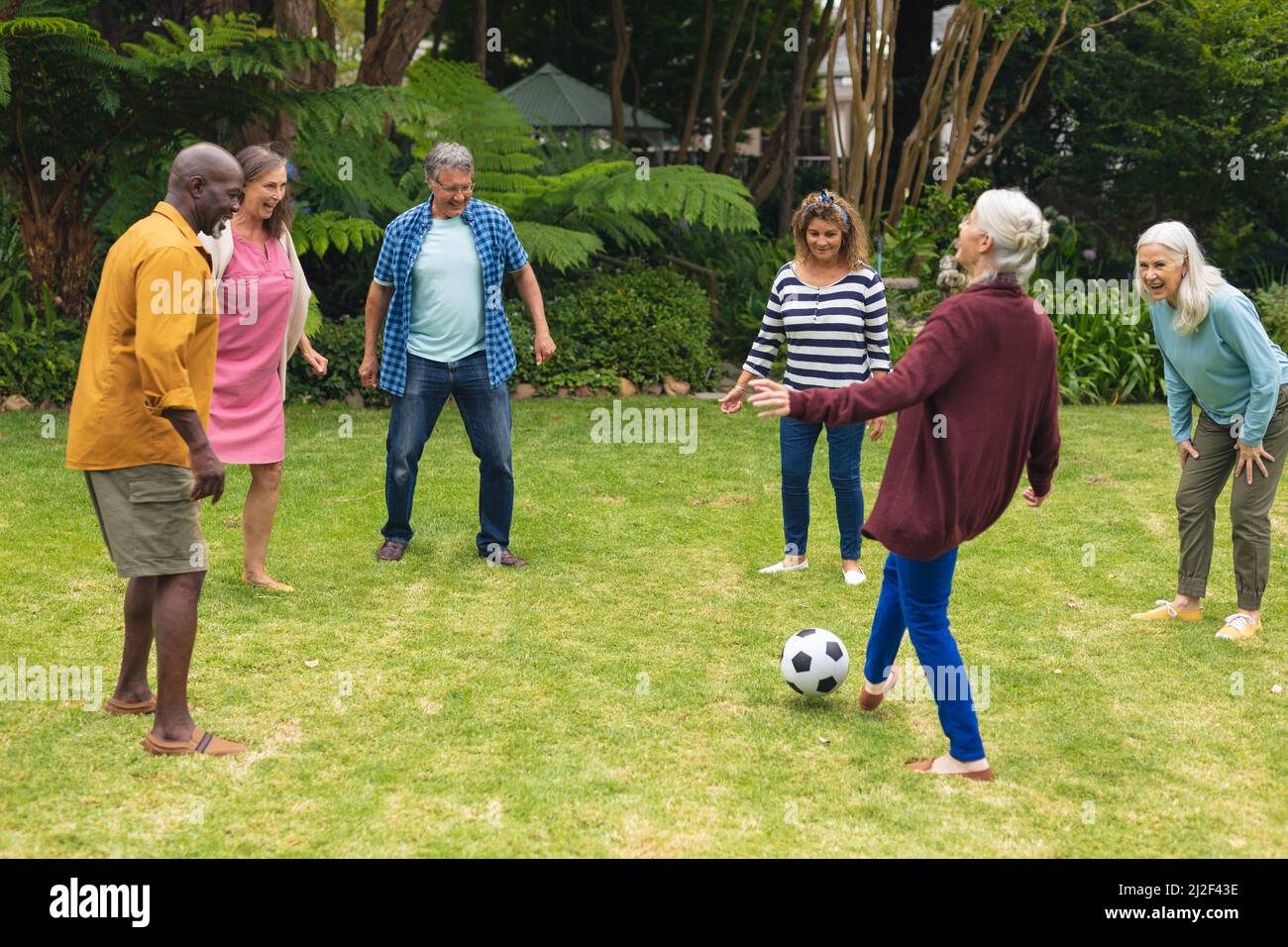 Multirassische aktive ältere männliche und weibliche Freunde, die am Wochenende gemeinsam im Hinterhof Fußball spielen Stockfoto