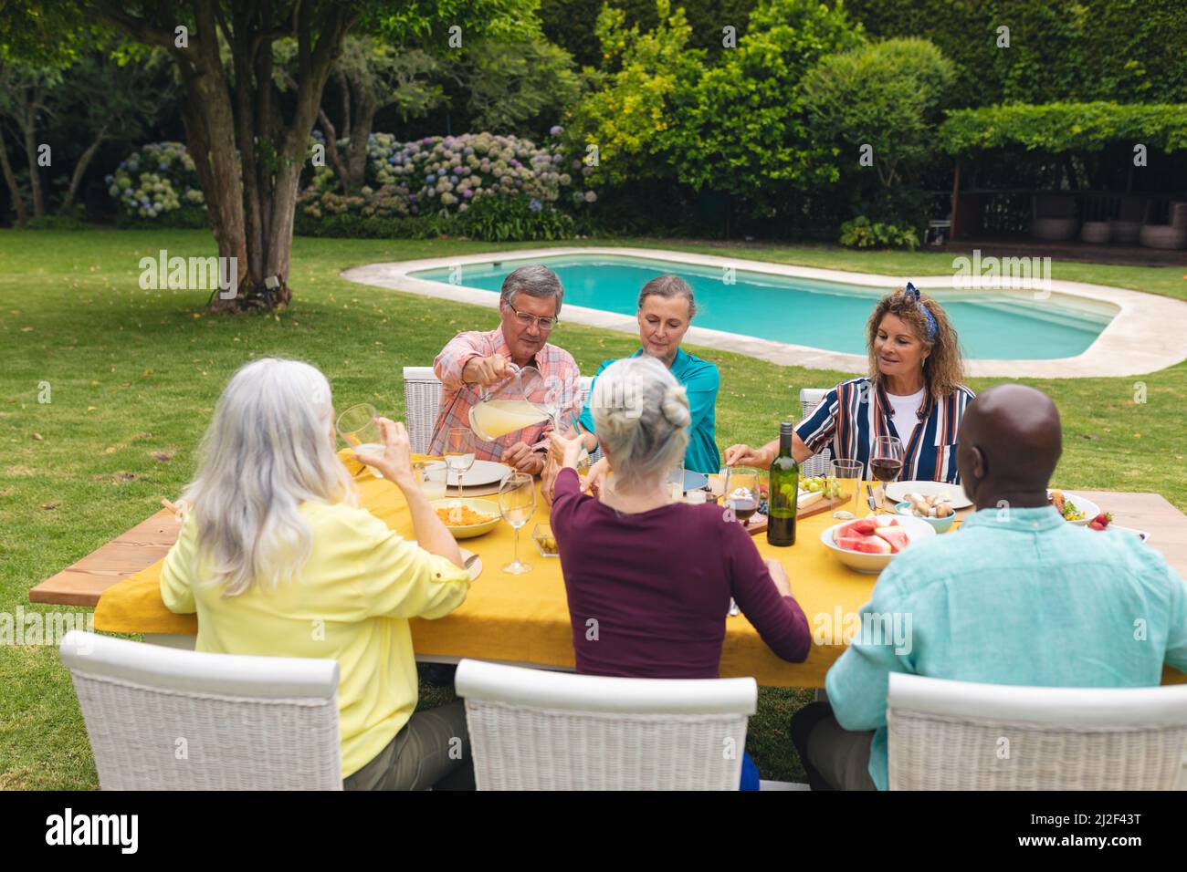 Mehrrassische ältere Männer und Frauen, die während der Hinterhofparty Essen am Tisch essen Stockfoto