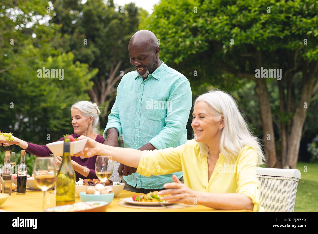 Multirassische ältere männliche und weibliche Freunde, die während der Hinterhofparty Wein am Tisch genießen Stockfoto