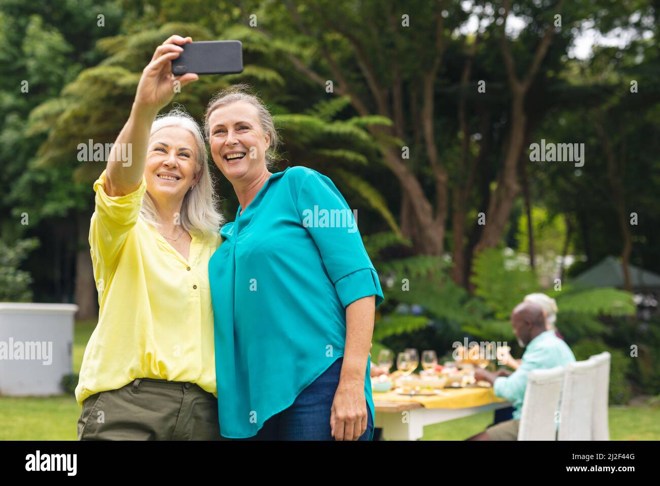 Glückliche kaukasische ältere Frauen, die während einer Hinterhofparty Selfie über das Smartphone machen Stockfoto