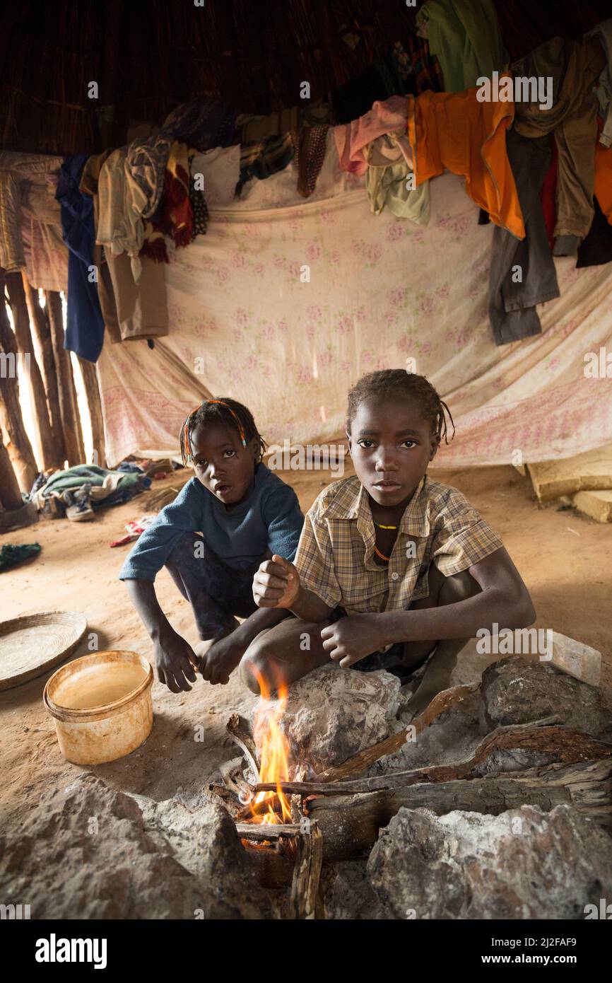 Drei Kinder wärmen sich am Feuer in ihrer ein-Zimmer-Hütte in der Region Omusati, Namibia, Südwestafrika. Stockfoto