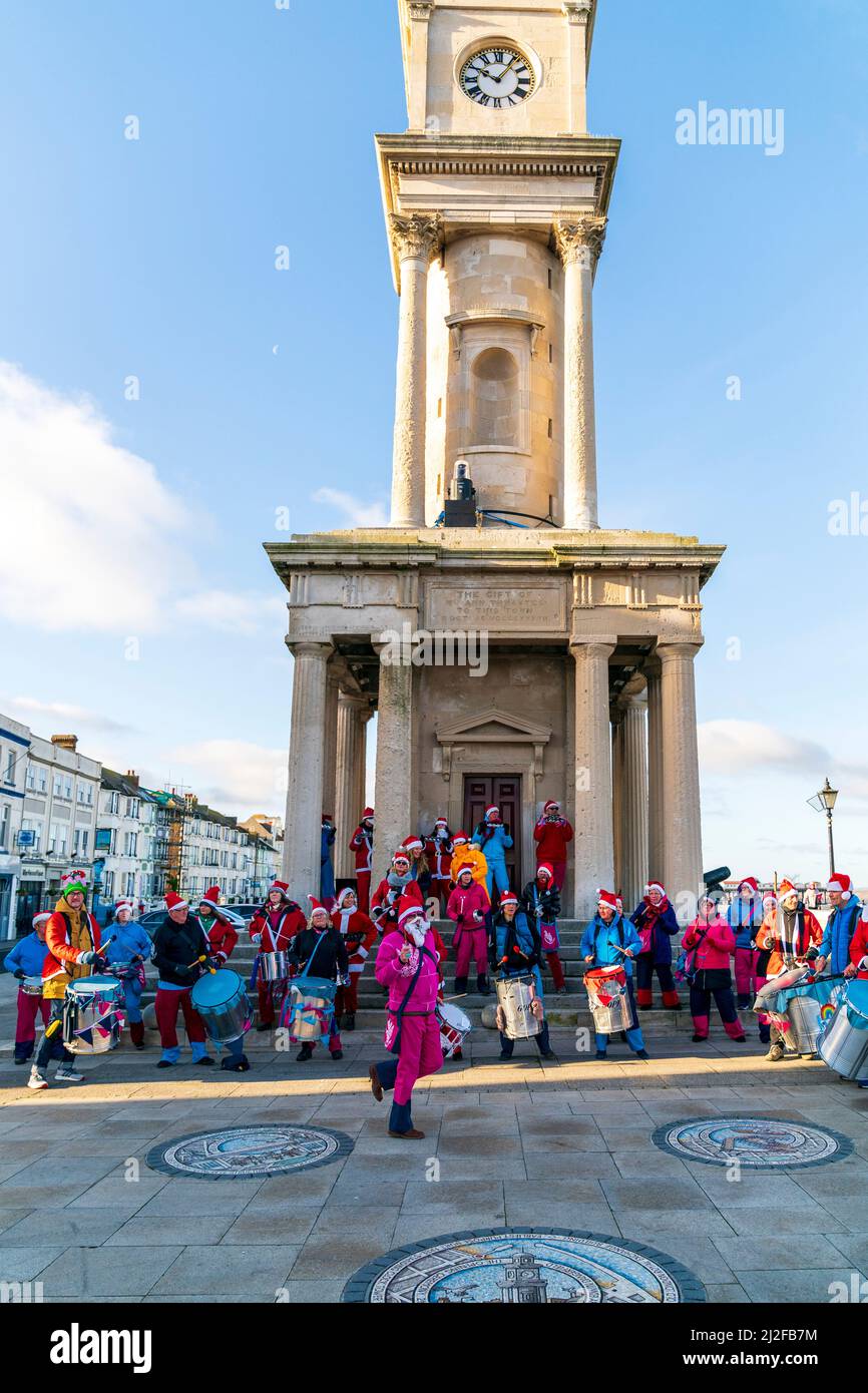 An einem kalten Wintertag zu Weihnachten tritt eine Percussion-Band vor den Steinstufen und Säulen des Herne Bay Uhrturms auf. Komprimierte Perspektive. Stockfoto