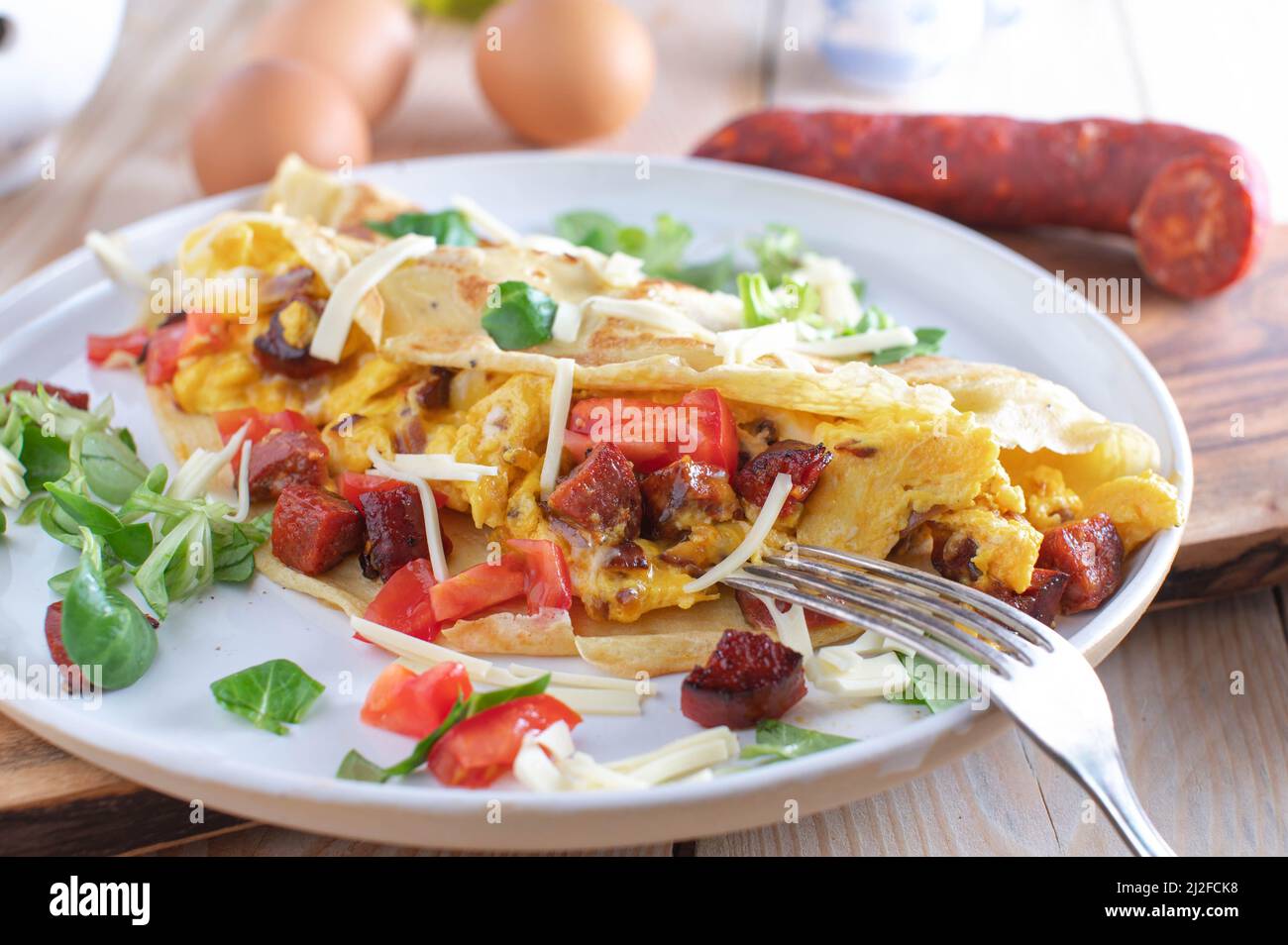 Crepe oder Pfannkuchen gefüllt mit Rührei, Tomaten, Käse und gebratener Chorizo-Salami. Serviert auf einem Teller für ein herzhaftes Frühstück Stockfoto