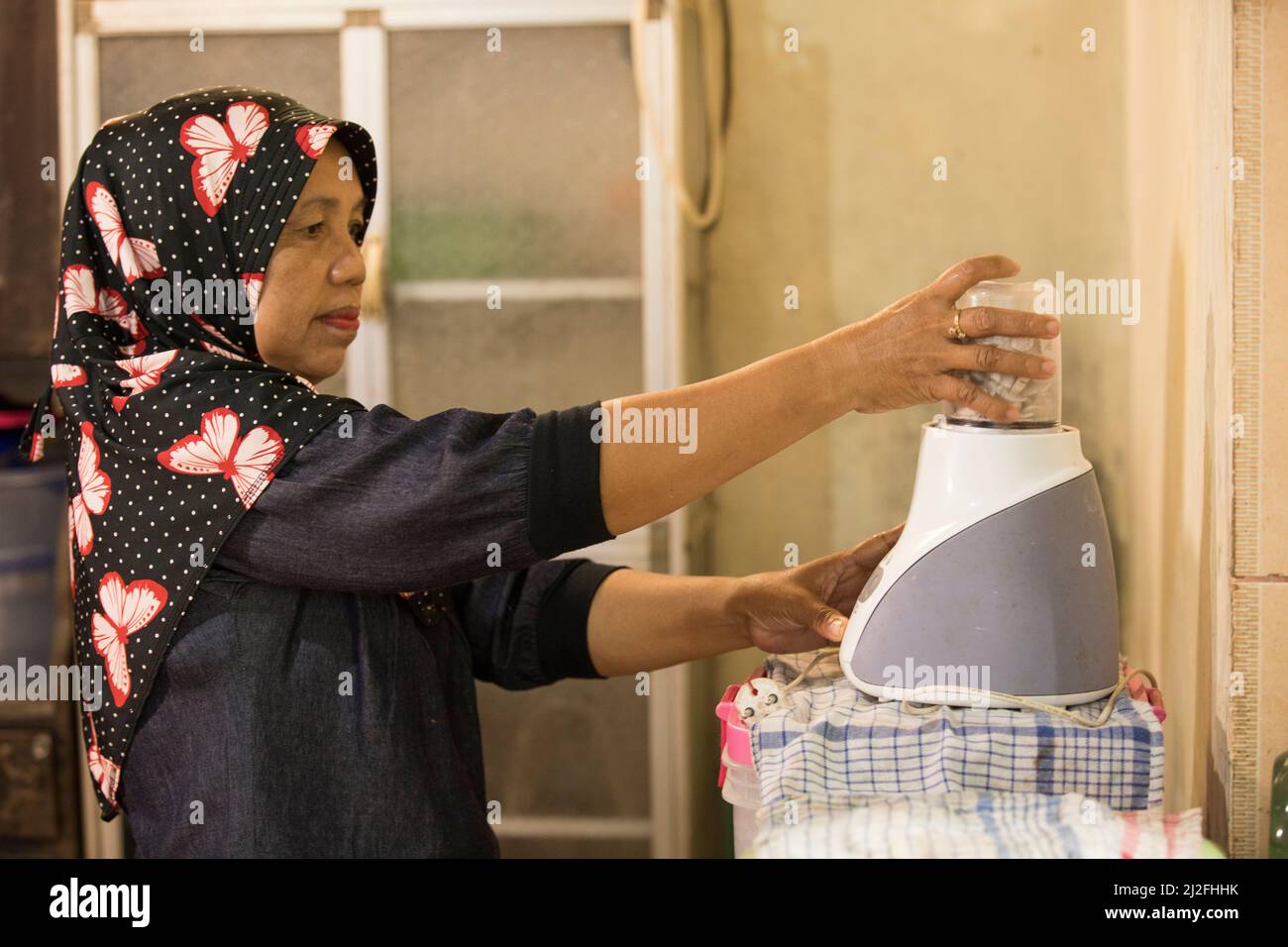 Eine Frau betreibt einen Mixer, während sie in ihrer Küche in West Sulawesi, Indonesien, Asien kocht. Stockfoto