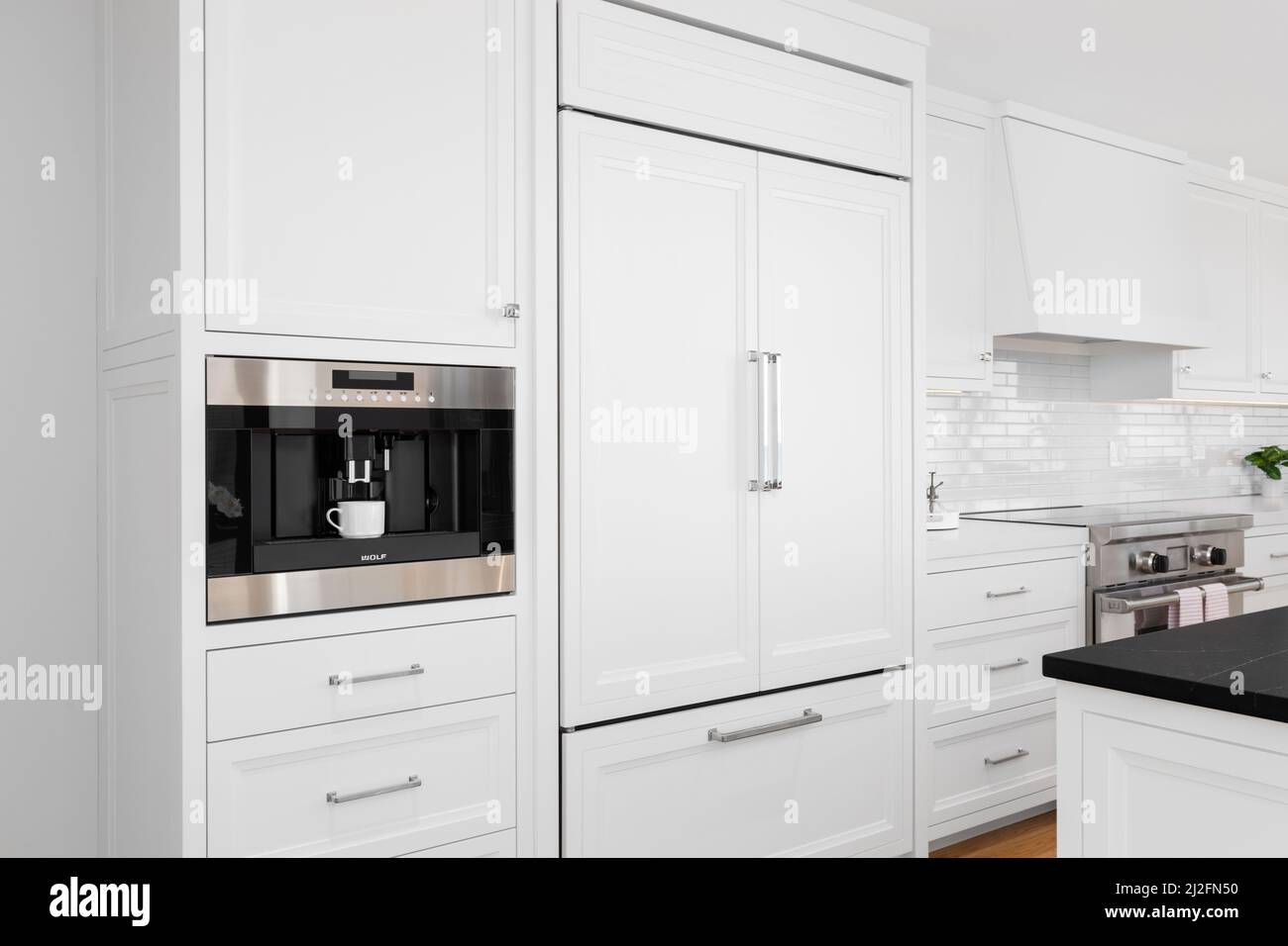 Eine weiße, luxuriöse Küche mit Sub-Zero-Kühlschrank und eingebauter Wolf-Kaffeemaschine. Stockfoto