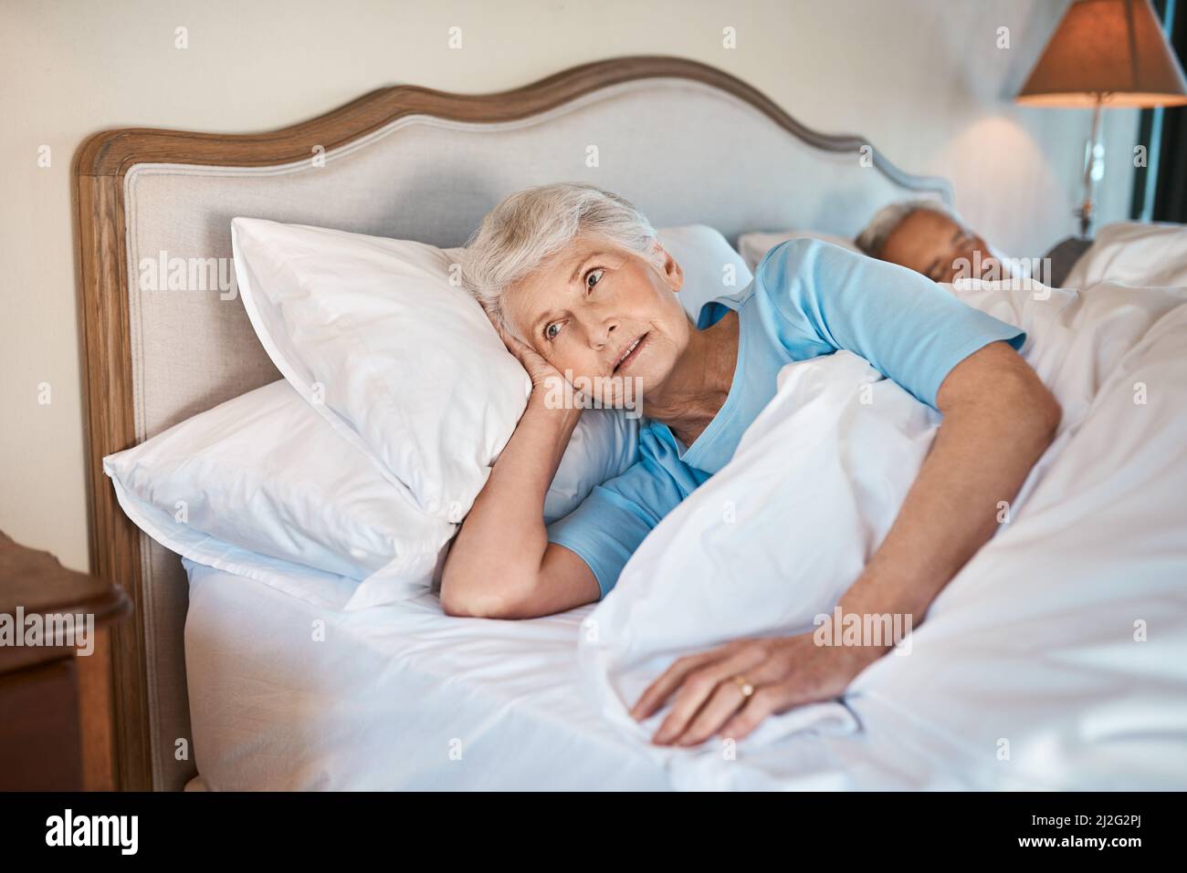 Ich denke an die Dinge, die ich heute tun muss. Zugeschnittene Aufnahme einer besinnlichen älteren Frau, die zu Hause neben ihrem schlafenden Mann im Bett liegt. Stockfoto