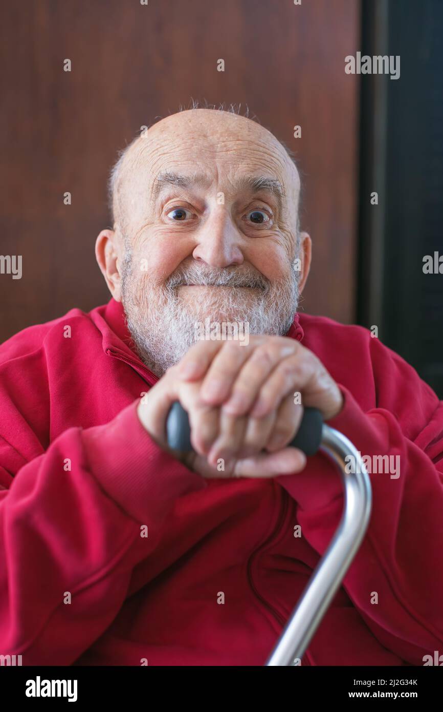 Lustiger alter Mann, der mit einem Gehstock in der Hand sitzt Stockfoto
