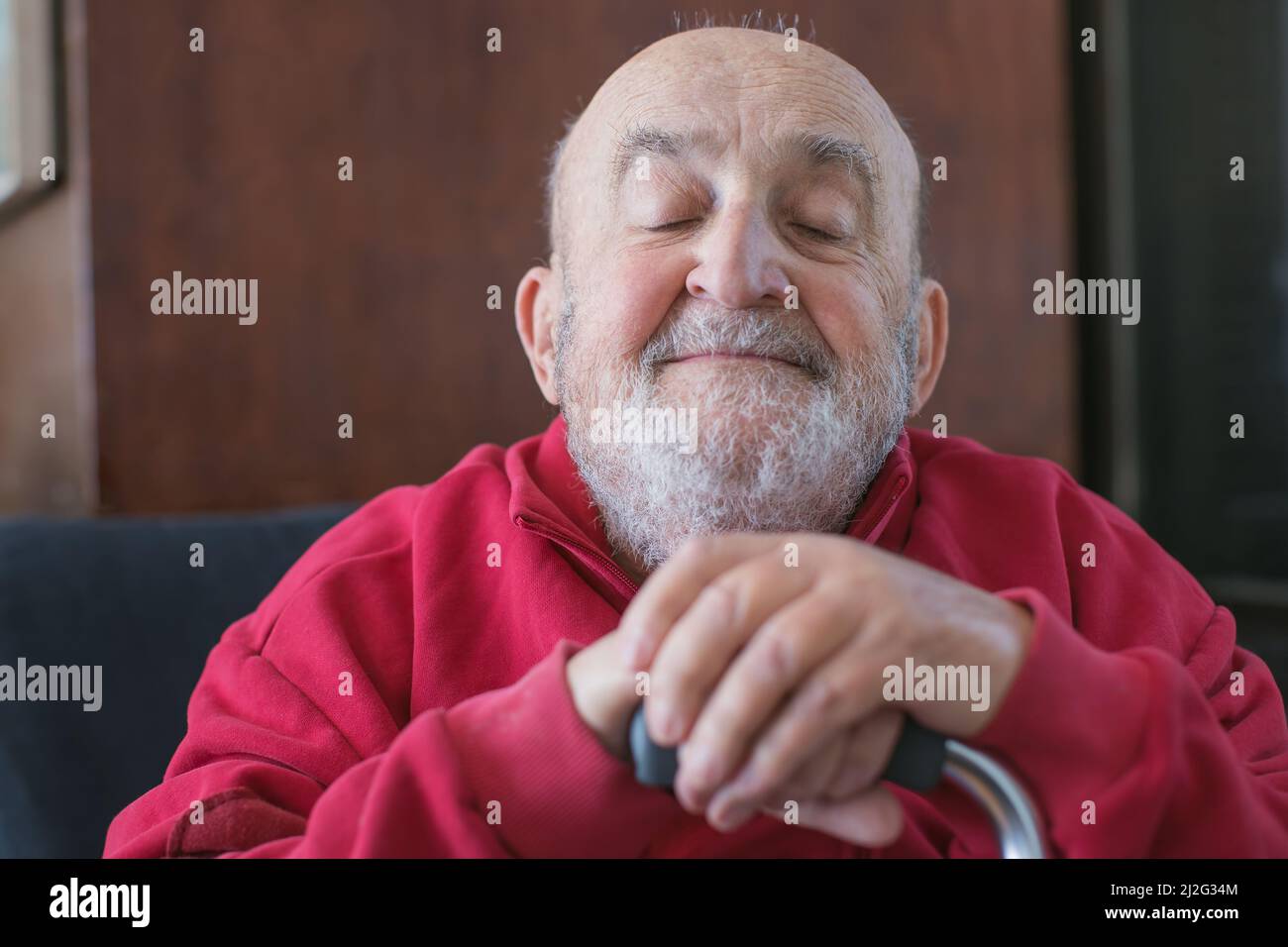 Alter Mann, der mit einem Gehstock in der Hand sitzt Stockfoto