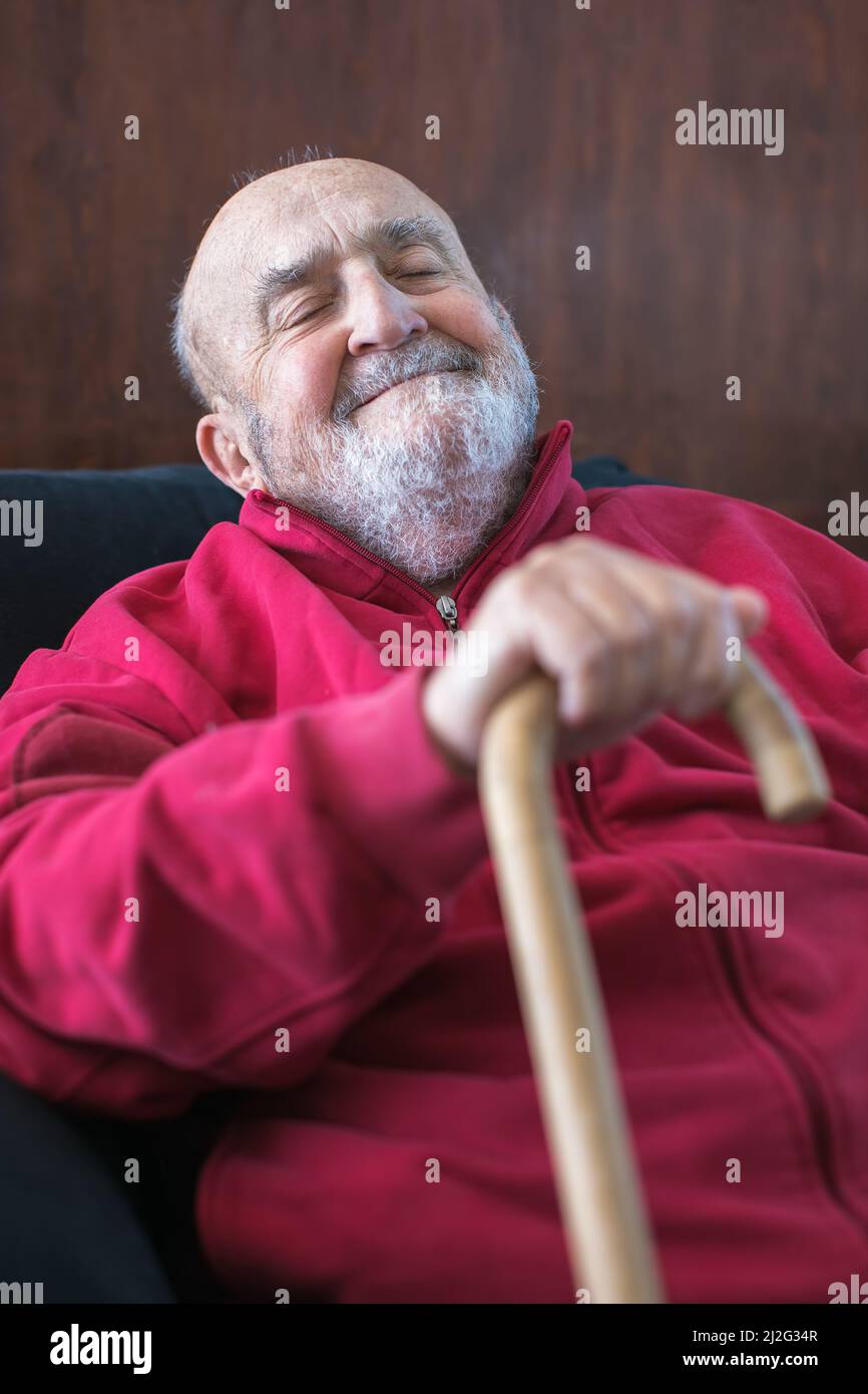 Älterer Mann, der mit einem Gehstock in der Hand sitzt Stockfoto