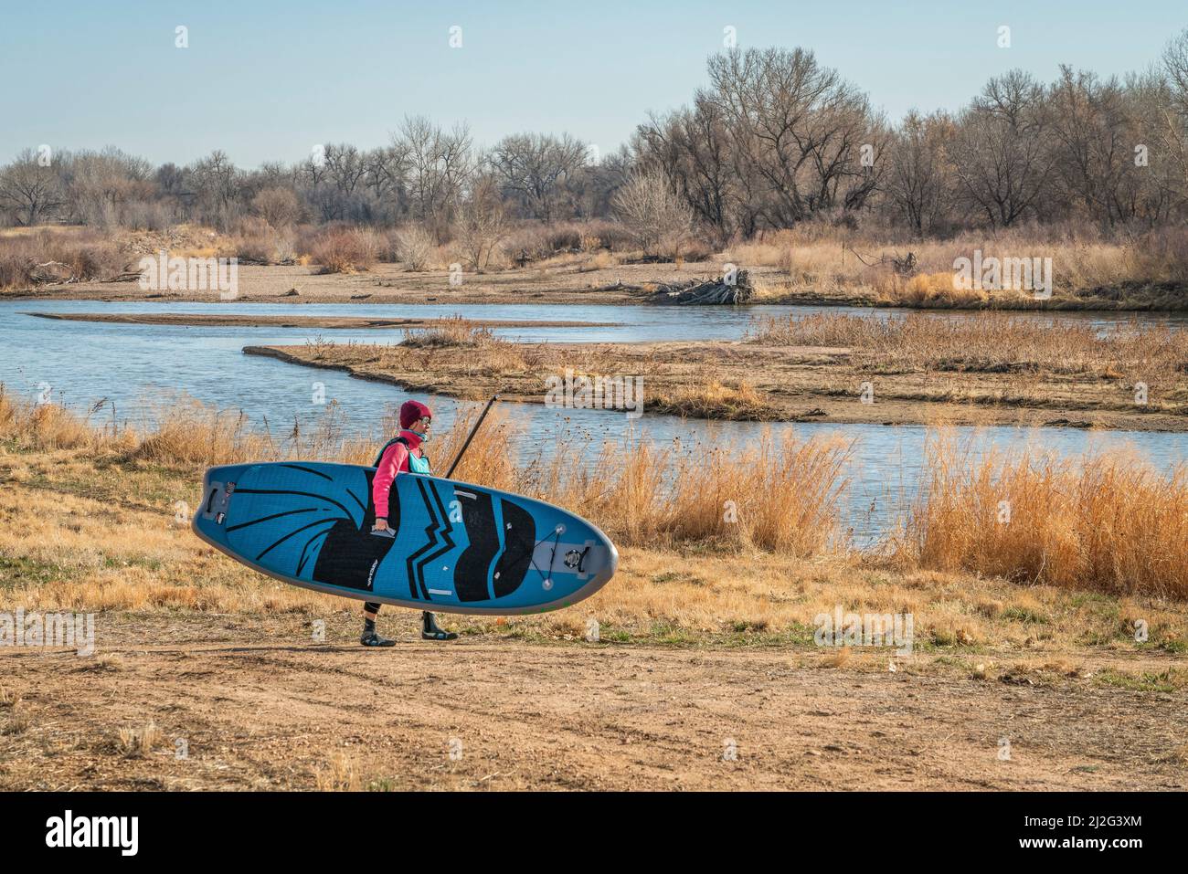 Evans, CO, USA - 26. März 2022: Die Paddlerin trägt ihr aufblasbares Stand Up Paddleboard, um für die Paddeltour im frühen Frühjahr in den Süden zu starten Stockfoto